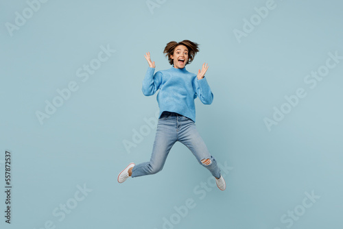 Full body overjoyed exultant excited young woman wear knitted sweater look camera jump high spread hands isolated on plain pastel light blue cyan background studio portrait People lifestyle concept.