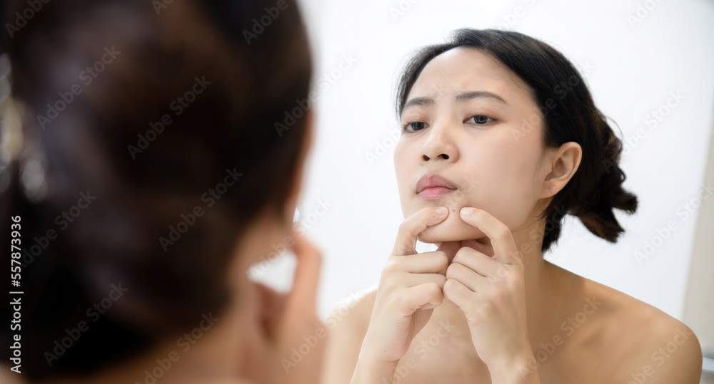 Problem skin. Concerned young asian women popping pimple on cheek while standing near mirror in bathroom. young asian women with acne Problem skin. Concerned young asian women popping pimple on cheek while standing near mirror in bathroom. young asian women with acne