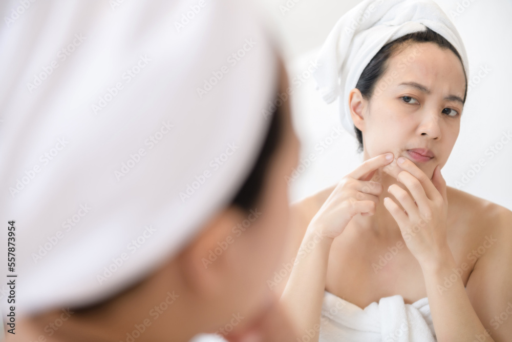 Problem skin. Concerned young asian women popping pimple on cheek while standing near mirror in bathroom. young asian women with acne Problem skin. Concerned young asian women popping pimple on cheek while standing near mirror in bathroom. young asian women with acne