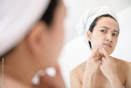 Problem skin. Concerned young asian women popping pimple on cheek while standing near mirror in bathroom. young asian women with acne photo