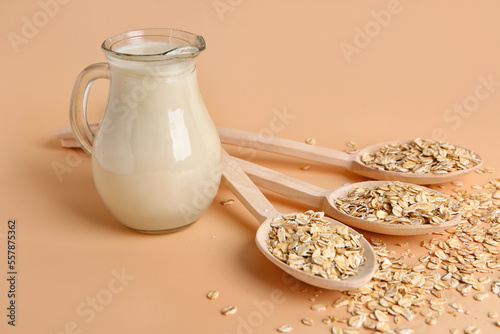 Spoons with raw oatmeal and jug of milk on color background