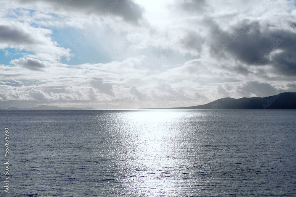 Sun beam reflection in the ocean . Low clouds over the island