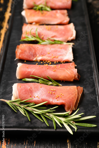 Plate with slices of tasty ham and rosemary on dark wooden background, closeup