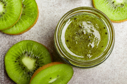 Homemade kiwi jam in a jar and kiwi slyces on concrete background with copy space