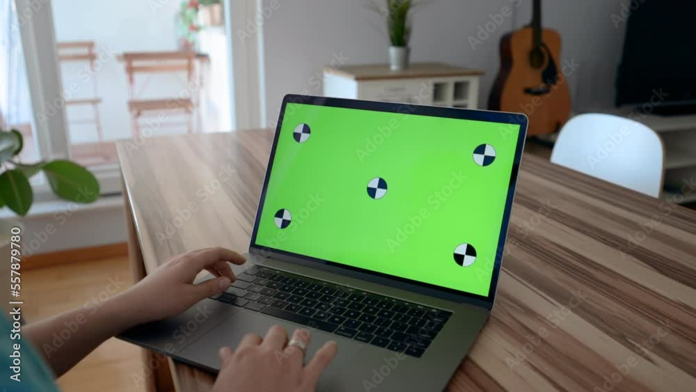 Hands of woman typing text on keyboard of electronic device with green chromakey screen. Female manager writes report on laptop at table closeup