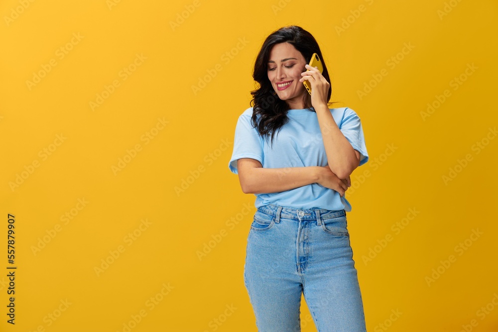 Woman blogger with a phone in her hands in a blue t-shirt and jeans on a yellow background smile signs gestures symbols, online communication and video call, copy space, free background Woman blogger with a phone in her hands in a blue t-shirt and jeans on a yellow background smile signs gestures symbols, online communication and video call, copy space, free background