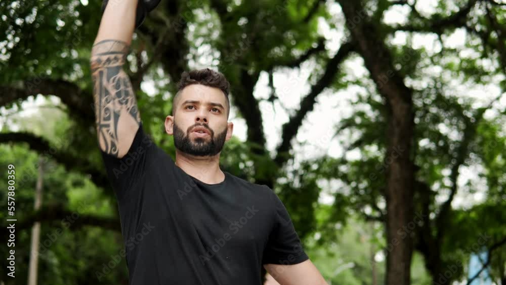 Motivated man in kettlebell shoulder workout in the park. Fit guy exercising upper body outside. Motivated man in kettlebell shoulder workout in the park. Fit guy exercising upper body outside.
