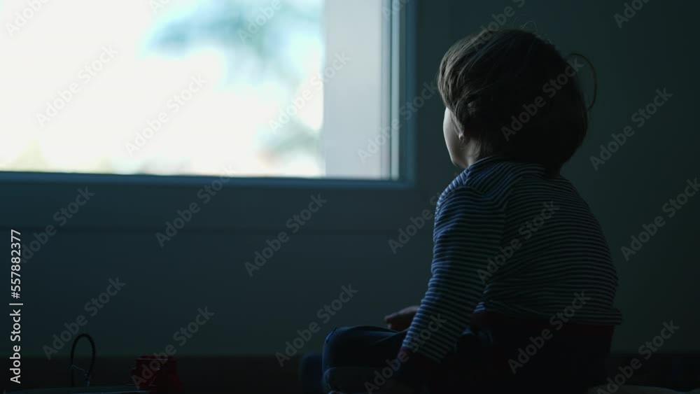 One lonely small boy sitting in the dark staring at window. Depressed child in bedroom alone