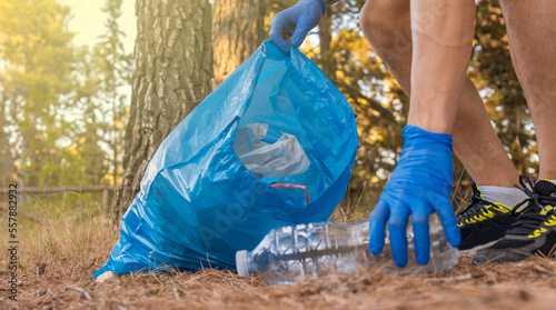 Detalle de brazo caucásico, con guantes de limpieza, recogiendo basura en la montaña, en día soleado.