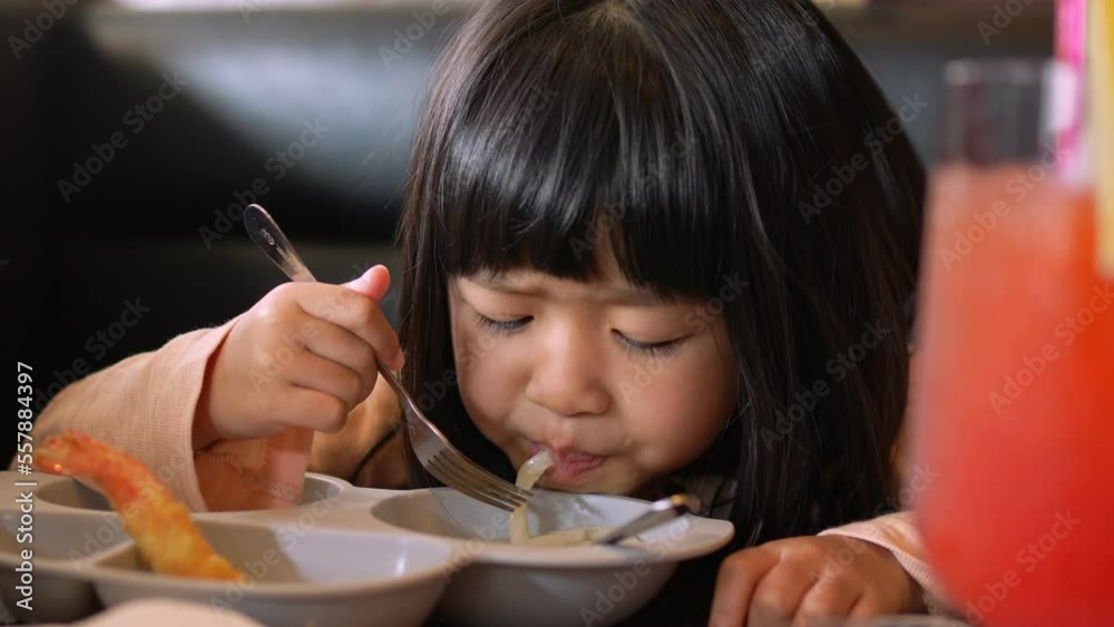 Asian girl sitting in the restaurant and eating Japanese noodles (Udon or ramen) and Shrimp Tempura with family and showing thumb up after eat. Tasty is very delicious. Childhood, health concept. Asian girl sitting in the restaurant and eating Japanese noodles (Udon or ramen) and Shrimp Tempura with family and showing thumb up after eat. Tasty is very delicious. Childhood, health concept.