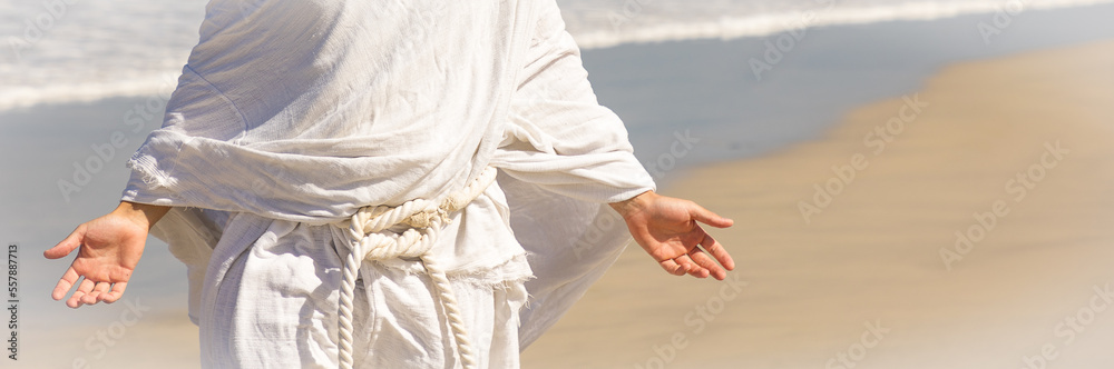 Christ-like man in white robe with open arms, closeup body shot next to sea