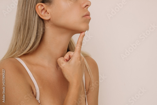 Cropped shot of young caucasian blonde woman pointing at her chin with her finger. Dimple on the chin isolated on a beige background. Mentoplasty concept