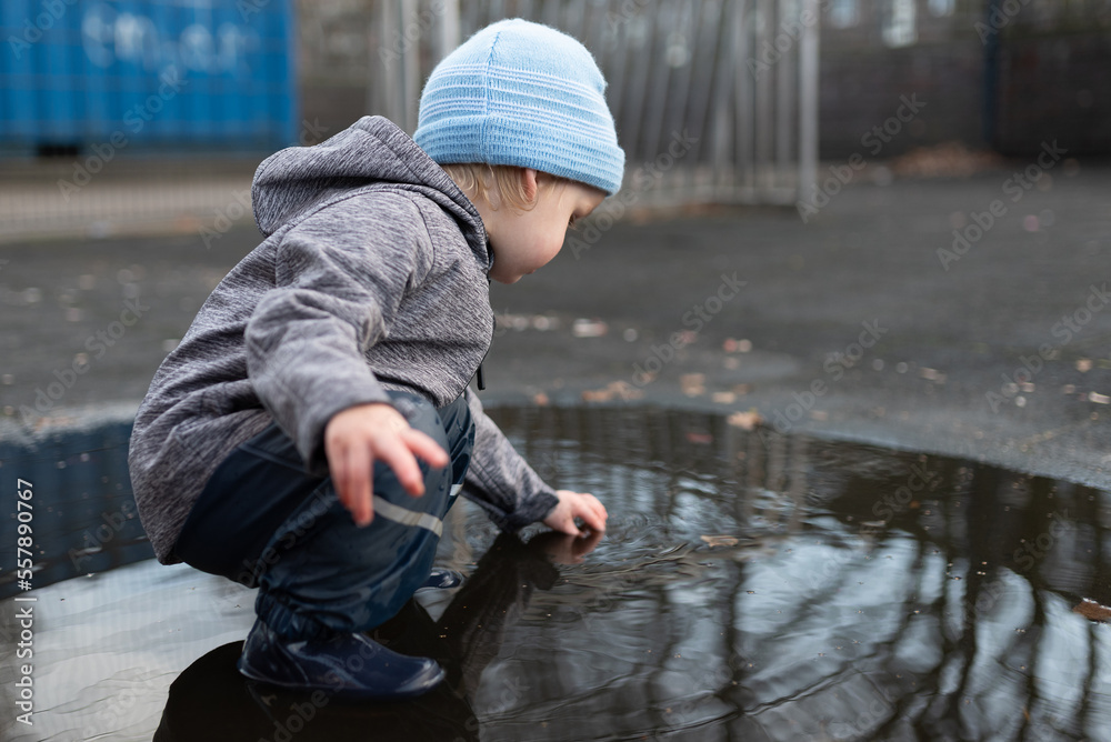 two year old boy in rain pants and rubber boots playing in puddle of water after rain shower two year old boy in rain pants and rubber boots playing in puddle of water after rain shower