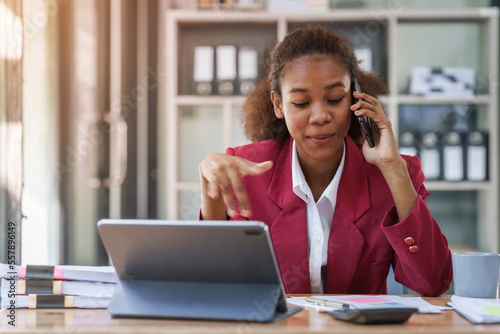 Young african american businesswoman red suit working at desk and using mobile smartphone in the modern office. Call a phone, operator.