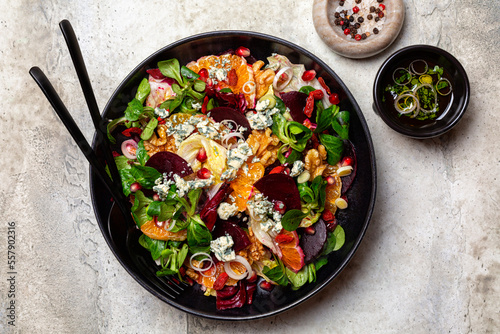 Winter salad with beetroot, oranges, walnuts, pomegranate, dried cranberries, valerian lettuce,  iceberg, onion and blue cheese. Healthy eating. Honey and olive oil dresseng. Above, light background.