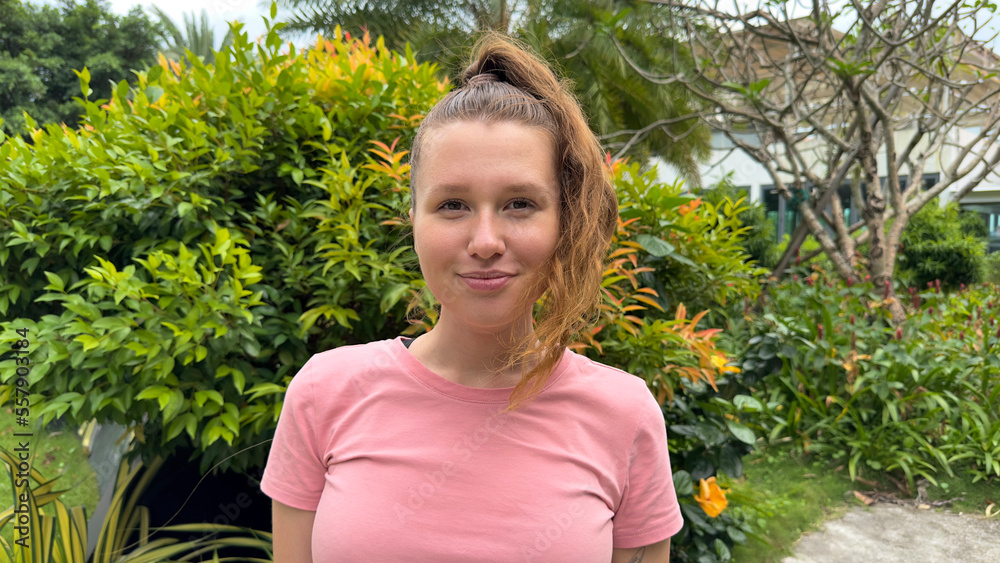 Portrait of a beautiful young woman standing on an Ivy wall or in greenery, smiling and looking away against from plant, girl relaxing outdoors during a sunny summer day. Love for nature, eco life