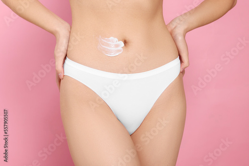 Woman with smear of body cream on belly against pink background, closeup