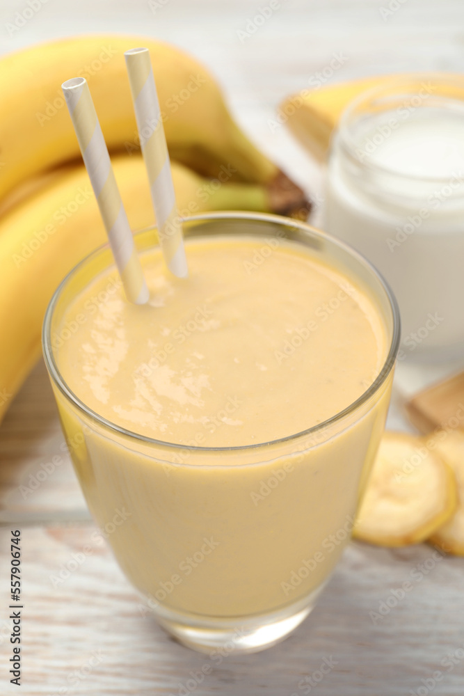 Glass of tasty banana smoothie with straws and ingredients on white wooden table, closeup Glass of tasty banana smoothie with straws and ingredients on white wooden table, closeup
