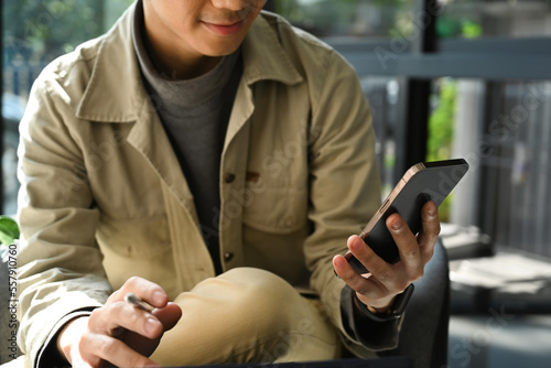 Cropped shot of smiling asian man sitting in outdoor coffee shop and using smart phone
