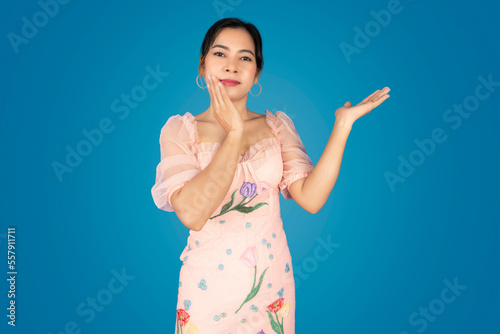 A beautiful woman stands with her left hand raised and her right hand pointing to her cheek