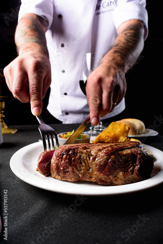 Propuesta gastronomica gourmet, lo mejor de la carne argentina. Bife de chorizo "a punto" servido directamente por las manos del chef, emplatado con acompañamientos y sobre una mesa de mantel negro. 