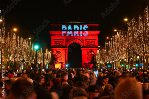 Paris, France - January 1st, 2023 : Crowd gathered on the Champs Elysées in Paris to celebrate the passing to 2023 with a fireworks show over the Arc de Triomphe (triumphal arch) photo