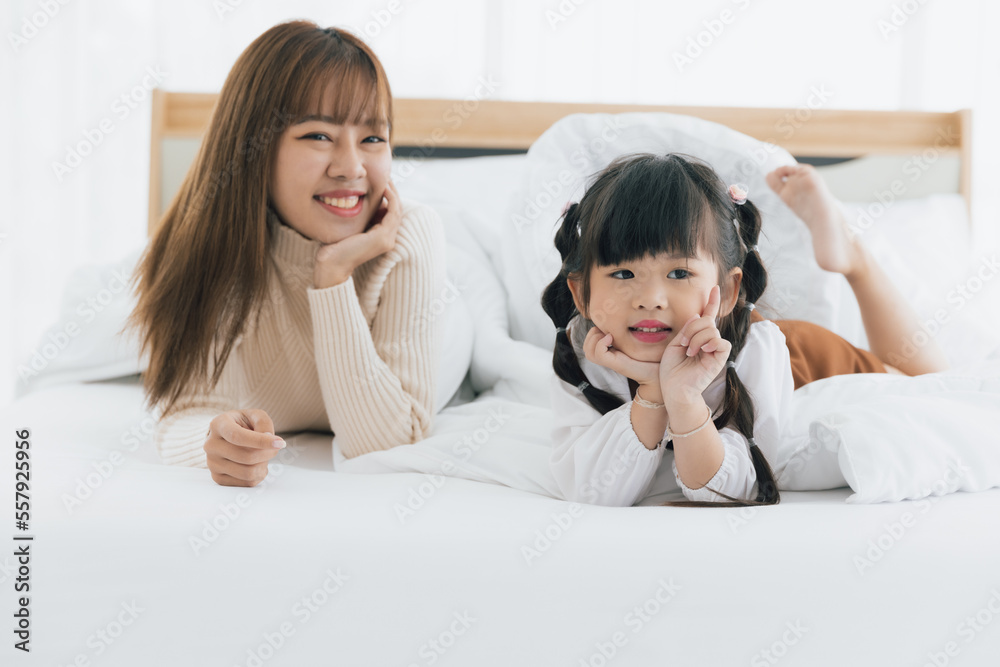 Young asian mother and 4years old kid daughter lying smiling and play together on white bed, Happy lovely family concept Young asian mother and 4years old kid daughter lying smiling and play together on white bed, Happy lovely family concept