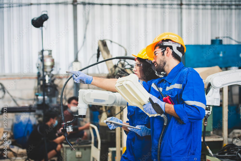 Engineers team mechanic using computer controller Robotic arm for welding steel in steel factory workshop. Industry robot programming software for automated manufacturing technology Engineers team mechanic using computer controller Robotic arm for welding steel in steel factory workshop. Industry robot programming software for automated manufacturing technology