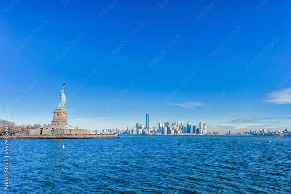 Statue of Liberty on Liberty Island and New York City Manhattan downtown skyline with skyscrapers and blue sky