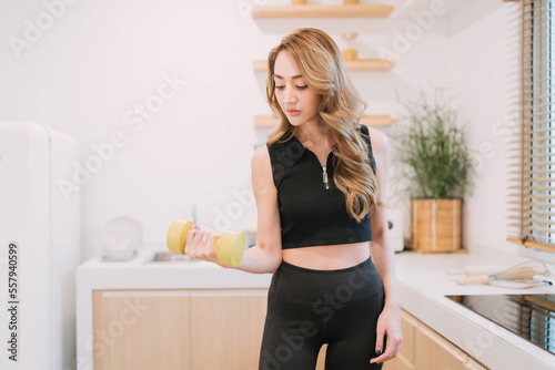 beautiful fitness woman using dumbbell exercising in kitchen. beautiful woman training holding light weight equipment follow home fitness trend. beautiful asian woman training in kitchen use dumbbell