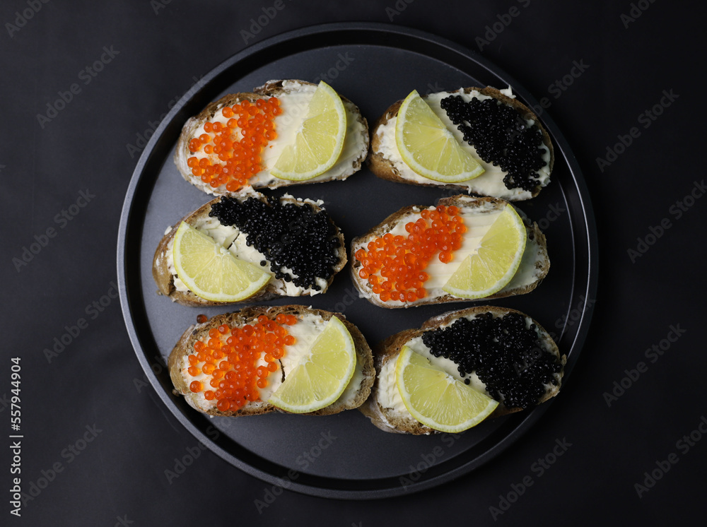 delicious fragrant sandwiches or bruschetta with melted cheese and black caviar and red caviar and lemon on a dark background. for splash screens labels flyers menu banners