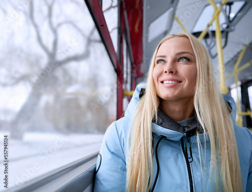 Fototapet Front view of beautiful blonde woman going home from work by bus in cold winter weather, happy, glad