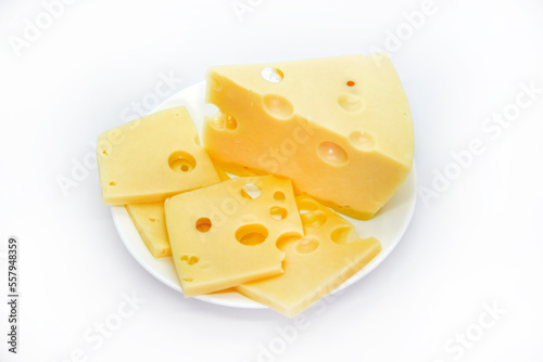 A large piece of cheese with holes on the plate. Chopped cheese and small slices on a white background. Juicy and delicious natural cheese. Cheese holes.