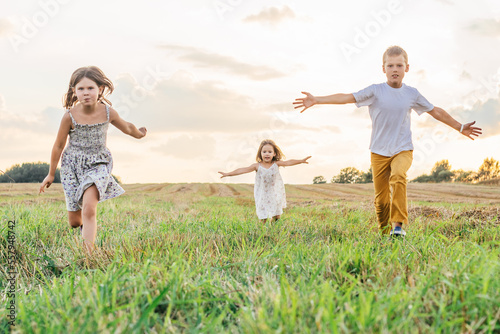 Happy little children run forward across field waving arms wide. Carefree kids on grassy meadow. Summer vacation.