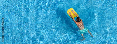 Boy child swim in swimming pool using board. Active wellness summer vacation in resort hotel. Water sports and game for children on summer holiday. Panoramic banner, copy space