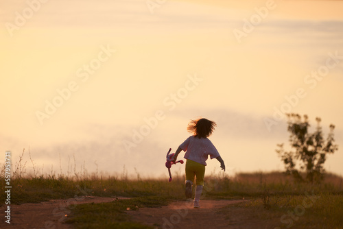 A child running along the trail with a doll in his hand at sunset. The little girl's hair was scattered.