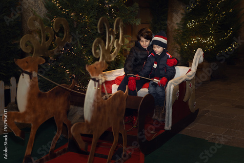Two boys brothers are sitting in Santa Claus sleigh. Winter holidays. Christmas miracle concept