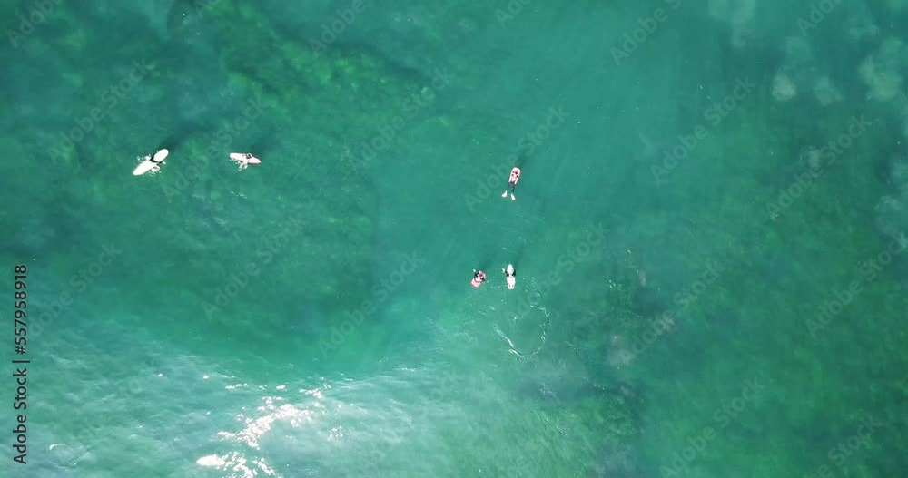 Aerial elevated zoom out over surfers and sun rays flowing through turquoise waves undulating above thriving marine life Aerial elevated zoom out over surfers and sun rays flowing through turquoise waves undulating above thriving marine life