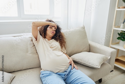 Pregnant woman sitting on the couch at home headache, pregnancy and motherhood difficulties, severe fatigue, headache