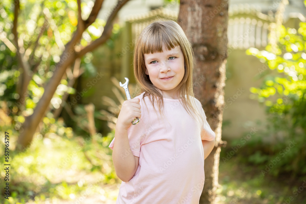 Young girl, elementary school age child posing holding a small metal wrench, outdoors shot, portrait, one person. Mechanic, jobs, occupations, freedom of choice, kids career dreams simple concept Young girl, elementary school age child posing holding a small metal wrench, outdoors shot, portrait, one person. Mechanic, jobs, occupations, freedom of choice, kids career dreams simple concept