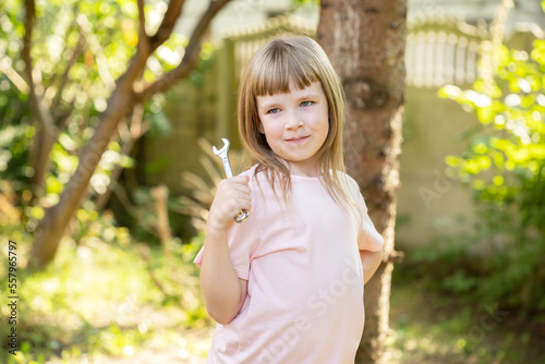 Young girl, elementary school age child posing holding a small metal wrench, outdoors shot, portrait, one person. Mechanic, jobs, occupations, freedom of choice, kids career dreams simple concept