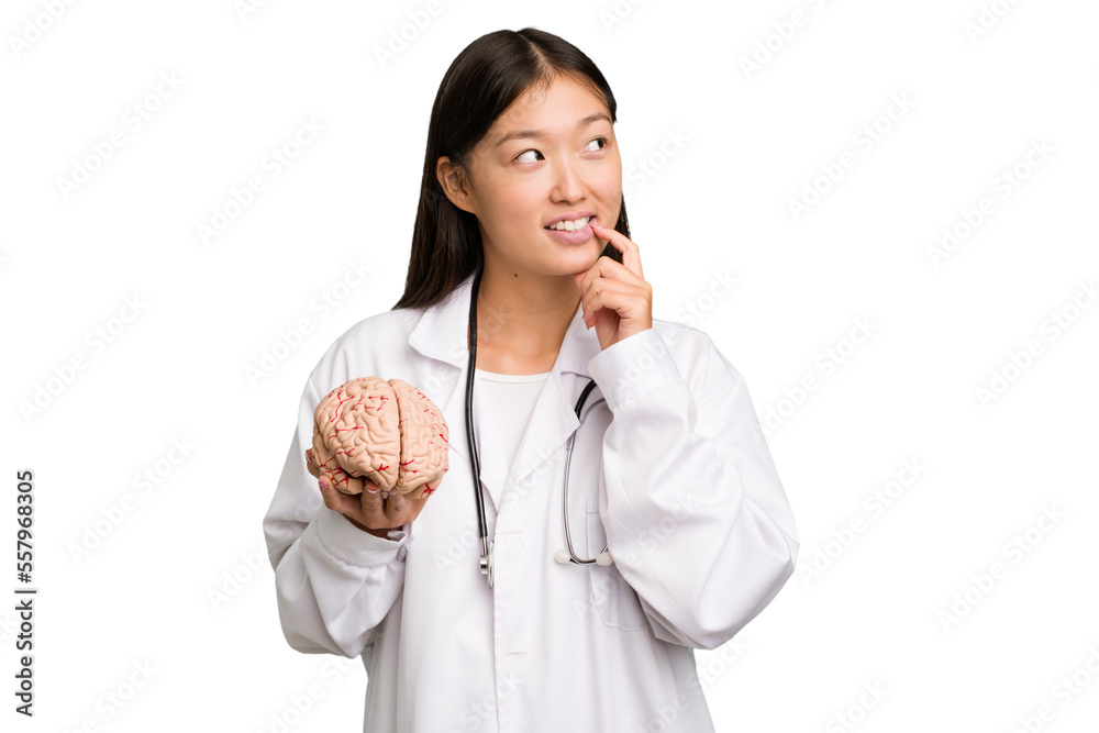 Young asian doctor woman holding a brain isolated relaxed thinking about something looking at a copy space. Young asian doctor woman holding a brain isolated relaxed thinking about something looking at a copy space.