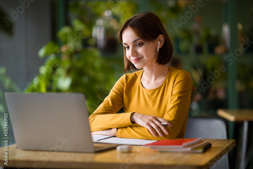 Cheerful young lady entrepreneur attending online business meeting, cafe interior