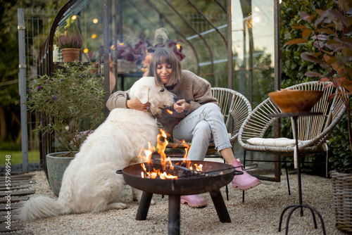 Young woman spends evening time with her cute white dog, sitting by the fire in garden at cozy and beautiful atmosphere photo