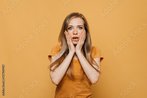Astounded speechless redhead woman in fear, reacts startled on breathtaking news about coronavirus, cannot believe in shocking statistics, wears bright yellow clothes, poses indoor. Emotions, reaction