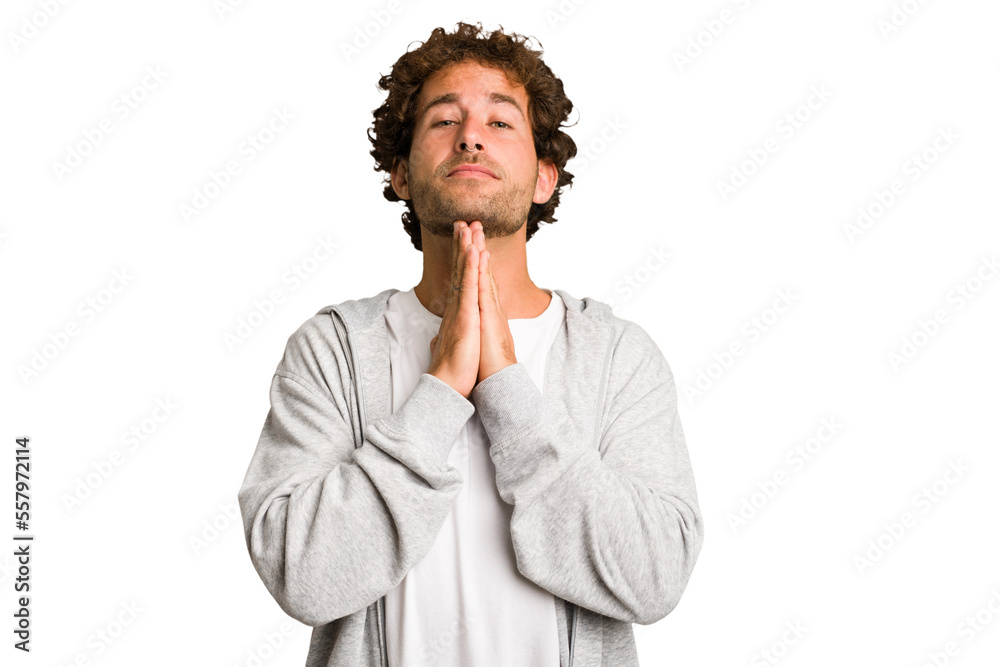 Young curly smart caucasian man cut out isolated holding hands in pray near mouth, feels confident.