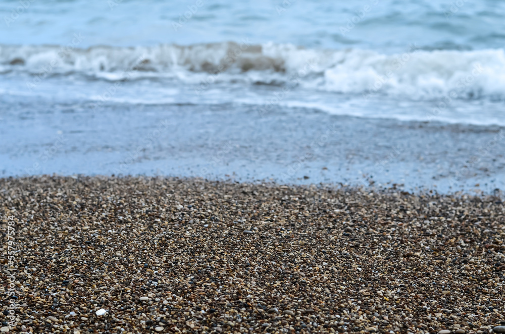 Small sea stones, pebbles on the seashore, splashes of water on the stones, background with wet stones, wet pebbles on the beach against the background of sea waves Small sea stones, pebbles on the seashore, splashes of water on the stones, background with wet stones, wet pebbles on the beach against the background of sea waves