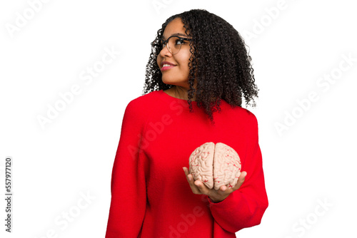 Young african american woman holding a brain model isolated looks aside smiling, cheerful and pleasant.