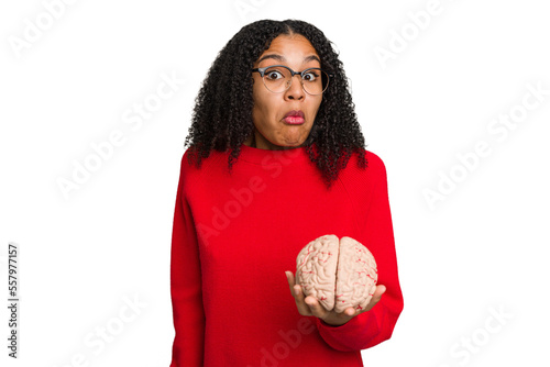 Young african american woman holding a brain model isolated shrugs shoulders and open eyes confused.