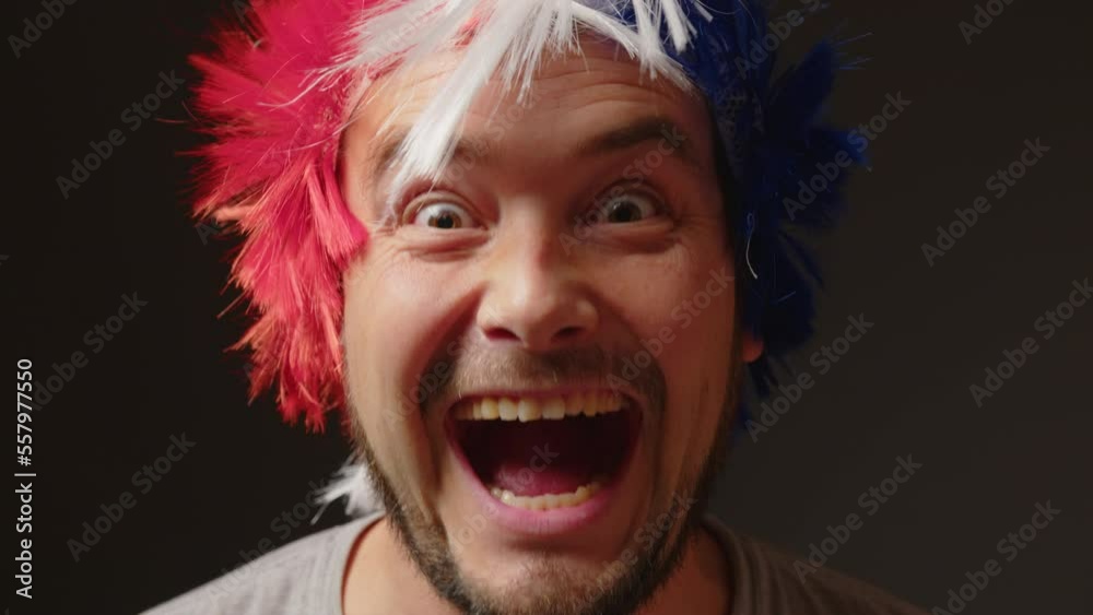 A man with a mohawk on his head in the colorful of the French flag supports his sports team. Football fan at the stadium rejoices at the victory of his team